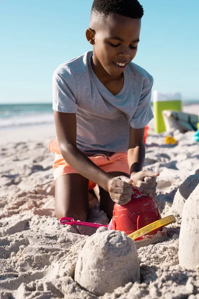 嬉闹的非洲裔美国男孩在沙滩上筑起一座沙堡 在晴朗的天空中衬托着水桶 复制空间 享受和夏季概念 — 图库照片