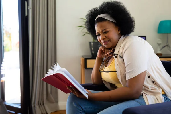 快乐又大的非洲裔美国女人坐在家里的扶手椅上看书 闲暇时间 家庭生活 身体包容和生活方式 — 图库照片