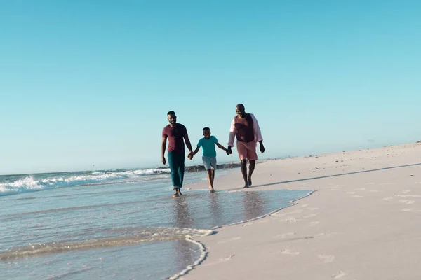 父と祖父の手を取り 澄んだ空の下で海岸を歩くアフリカ系アメリカ人の少年 コピースペース 変更されていない 多世代家族 一緒に 子供時代 楽しみ — ストック写真