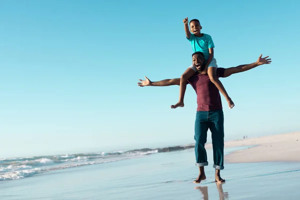 空の下の海岸で子供を肩に担いで腕を伸ばして陽気なアフリカ系アメリカ人男性 コピースペース 変更されていない 一緒に 子供時代 楽しみと夏 — ストック写真