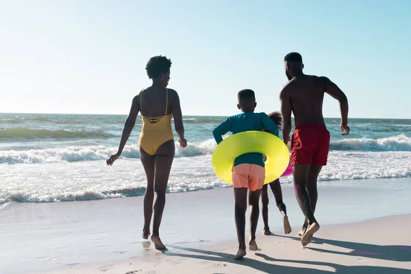 海岸を走るスイミングフロートを持つ陽気なアフリカ系アメリカ人の両親と子供の後ろの景色 コピースペース 変更されていない 一緒に ビーチ 楽しみ — ストック写真