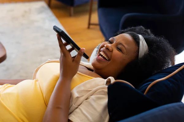 Щаслива Велика Афро Американська Жінка Лежить Дивані Розмовляє Смартфону Сміється — стокове фото