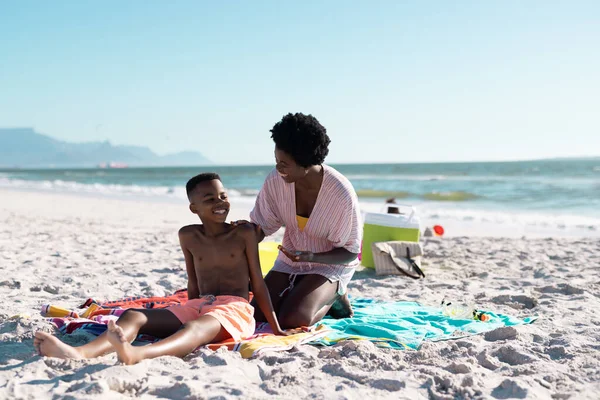 アフリカ系アメリカ人の女性は 澄んだ空に対してビーチでの子供の体に日焼け止めを適用します コピースペース 変更されていない 一緒に スキンケア 楽しみ — ストック写真