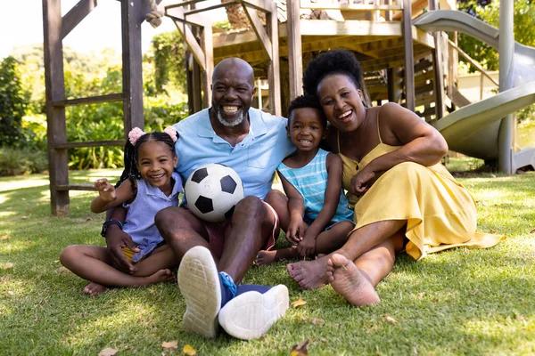 公園の芝生の土地に座ってボールと陽気なアフリカ系アメリカ人の祖父母と孫 変更されていない 一緒に 子供時代 スポーツ 引退した サッカー 楽しさと週末のコンセプト — ストック写真