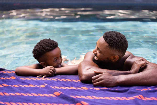 非裔美国人的父亲和儿子赤身裸体地相互望着对方 并在度假胜地的湖边依偎着 不变的家庭 夏天和周末的概念 — 图库照片