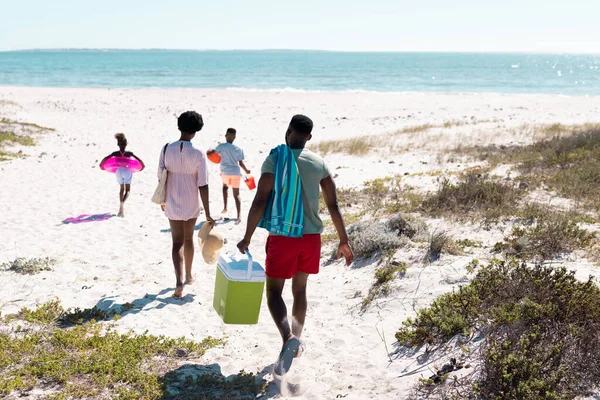 スイミングフロートを備えたアフリカ系アメリカ人の家族の後ろの景色 海に向かってビーチを歩くクーラー コピースペース 変更されていない 一緒に 子供時代 ピクニック 楽しみ — ストック写真