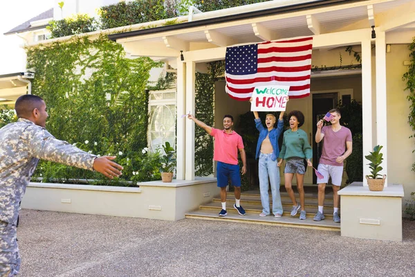 stock image Happy diverse group of friends greeting biracial male american soldier outside the house. American flag, homecoming, patriotism and military service.