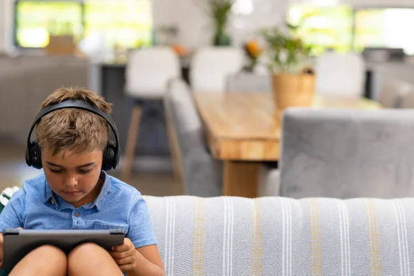 白人男孩头戴耳机 在客厅沙发上休息时使用数字平板电脑 不变的生活方式 技术和家庭观念 — 图库照片