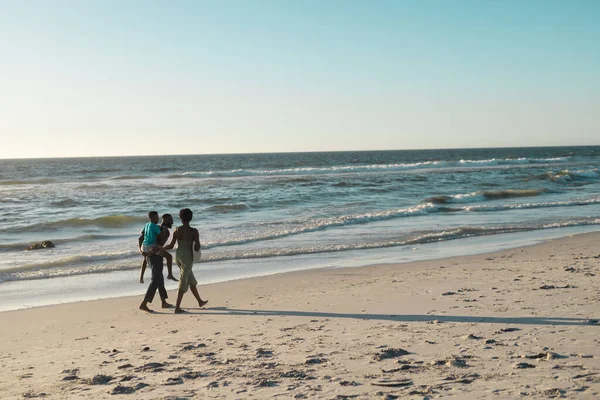 アフリカ系アメリカ人のピギーバックの息子と空に対して美しい海でビーチで妻と歩く コピースペース 変更されていない 一緒に 子供時代 楽しさと夏のコンセプト — ストック写真