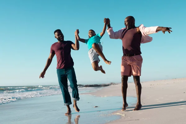 アフリカ系アメリカ人の父と祖父は少年の手を握り 空の下でビーチで彼を拾う コピースペース 変更されていない 多世代家族 一緒に 子供時代 楽しみ — ストック写真