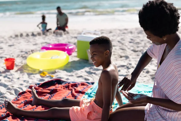 Африканська Мама Американка Сидячи Пляжі Наносить Сонцезахисний Крем Тіло Сина — стокове фото
