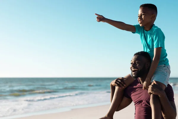Веселий Афроамериканець Несе Сина Плечі Вказуючи Пляж Проти Моря Неба — стокове фото