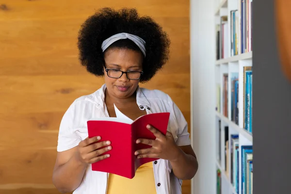 快乐又大的非洲女人 戴着眼镜 站在书架上看书 家庭生活 身体包容和生活方式 — 图库照片