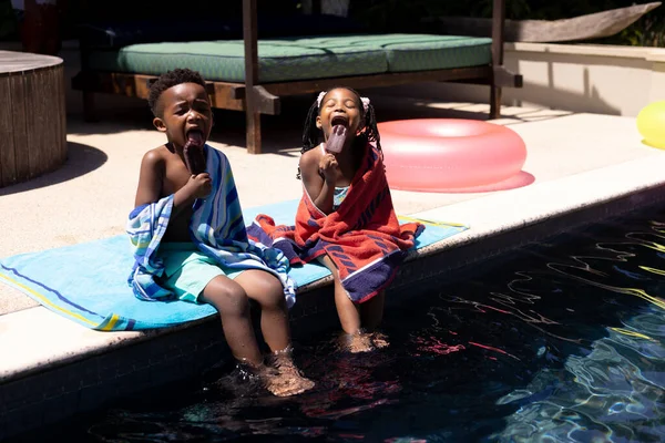夏にリゾートのプールサイドに座っている間 アフリカ系アメリカ人の兄と妹はアイスクリームを食べています 変更されていない 子供時代 食べ物 楽しみと週末のコンセプト — ストック写真