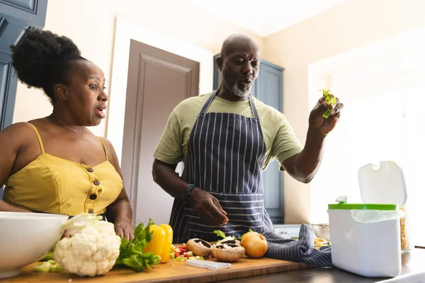 快乐的资深非洲裔美国夫妇穿着围裙 把垃圾扔在厨房里 老年人的生活方式 食物和家庭生活 — 图库照片