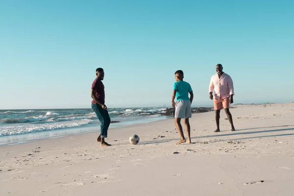 アフリカ系アメリカ人の少年は澄んだ空を背景にビーチで父親と祖父とサッカーをしている コピースペース 変更されていない 多世代家族 一緒に 小児期 楽しみ — ストック写真