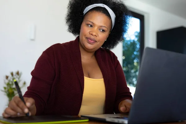 快乐加尺寸的非洲裔美国女人坐在桌旁 使用笔记本电脑和绘图平板电脑 在家工作 身体包容和生活方式 — 图库照片