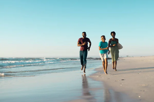 アフリカ系アメリカ人の父と母は澄んだ空に向かって海岸で遊び心のある息子の後ろを走っていた コピースペース 変更されていない 一緒に 子供時代 楽しさと夏のコンセプト — ストック写真