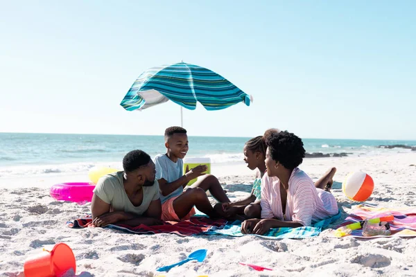 アフリカ系アメリカ人の子供たちは 空に対して砂浜でリラックスしながら両親と話をします コピースペース 変更されない 一緒に 子供時代 ピクニック パラソル 楽しみと夏 — ストック写真