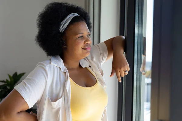 思考プラスサイズアフリカ系アメリカ人の女性が窓や笑顔を通して見て 国内生活 身体的包容力と生活様式 変更なし — ストック写真