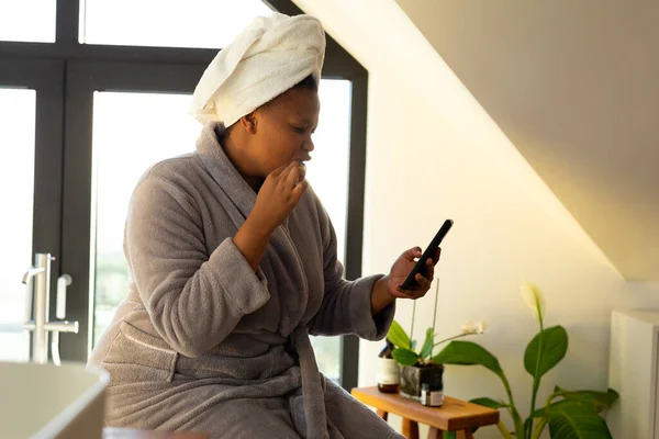 Συν Μέγεθος Αφροαμερικανή Γυναίκα Φορώντας Ρόμπα Χρησιμοποιώντας Smartphone Στο Μπάνιο — Φωτογραφία Αρχείου