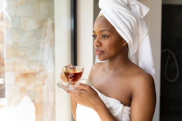 快乐的非洲裔美国人穿着毛巾 在浴室里端着一杯茶 独自待在家里的质量时间 家庭生活和生活方式概念 — 图库照片