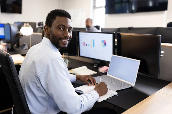 Happy african american man working on laptop in office. Business, corporation, cooperation and working in office concept.