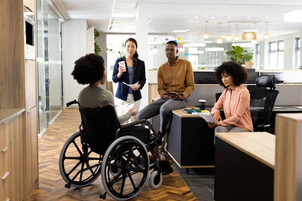 African american businesswoman on wheelchair and diverse people in office talking and laughing. Business, corporation, working in office concept.