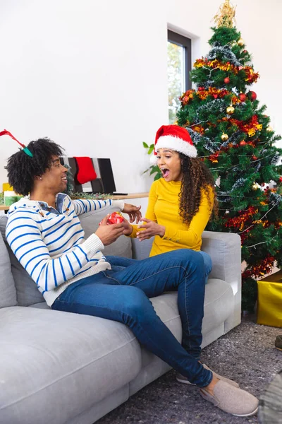 幸せなアフリカ系アメリカ人のカップルのリビングルームとアンパックプレゼントでソファに座っている 一緒にクリスマスに質の高い時間を過ごす — ストック写真