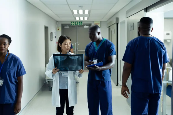 Diverse female doctor and male healthcare worker discussing x-ray photo in busy hospital corridor. Hospital, medical and healthcare services.