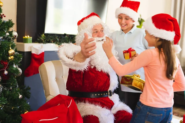 サンタクラスの白人の子供たちはクリスマスプレゼントを与えます クリスマス 家族の時間とお祝いの概念 — ストック写真