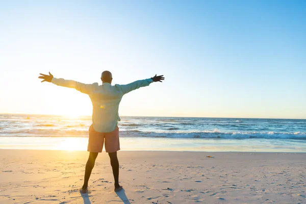 青い空に対して海を見て腕を伸ばしてアフリカ系アメリカ人のシニア男性の背面ビュー 夕暮れ コピースペース 屈託のない 幸せな 変更されていない ビーチ 楽しみ — ストック写真