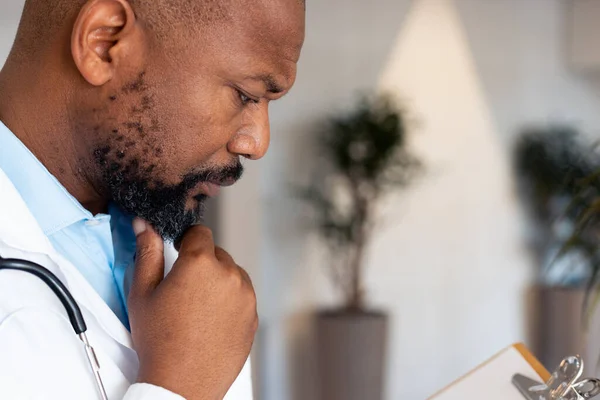 病院の廊下でクリップボードにメモを読んでいるアフリカ系アメリカ人男性医師の思考 医療サービス — ストック写真