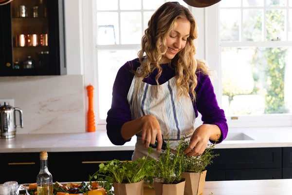 Усміхнена Біла Жінка Стоїть Кухні Фартусі Вирізаючи Свіжі Трави Кухонними — стокове фото
