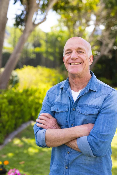 青いシャツを着て庭に立っているシニア白人男性の垂直肖像画 引退後は一人で外で過ごす — ストック写真