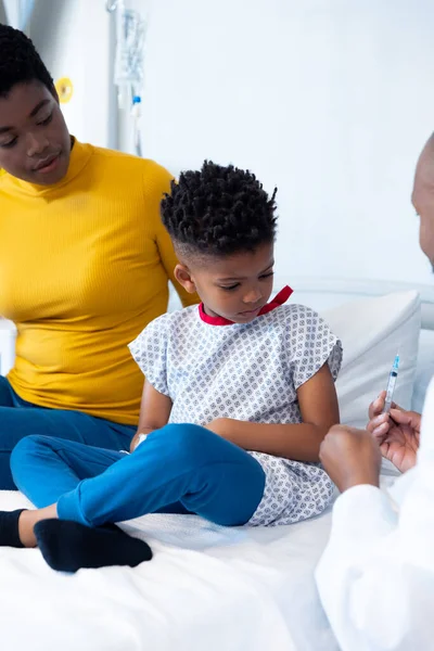 母親とコピースペースを持つ少年患者にワクチンを示すアフリカ系アメリカ人男性医師の垂直 医療サービス — ストック写真