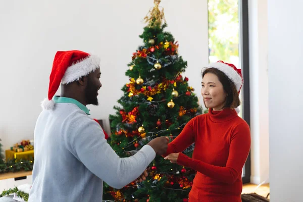 クリスマスツリーの隣で踊って サンタの帽子をかぶって幸せな多様なカップル 一緒にクリスマスに質の高い時間を過ごす — ストック写真