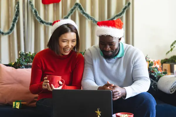 快乐多样的夫妇戴着圣塔克洛斯帽 使用笔记本电脑进行视频通话 在圣诞佳节一起共度美好时光 — 图库照片