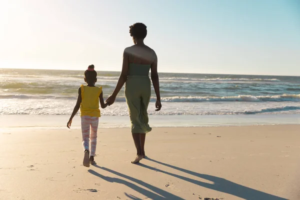 アフリカ系アメリカ人の母親と娘が手を取り合い 空の下で海に向かって歩く様子 コピースペース 変更されていない 一緒に ビーチ 子供時代と自然コンセプト — ストック写真