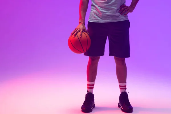 Image of low section of biracial basketball player with basketball on neon purple background. Sports and competition concept.