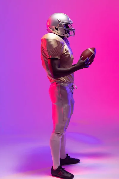 Afroamerykanin Mężczyzna Amerykański Piłkarz Trzyma Piłkę Neonem Fioletowy Różowe Oświetlenie — Zdjęcie stockowe