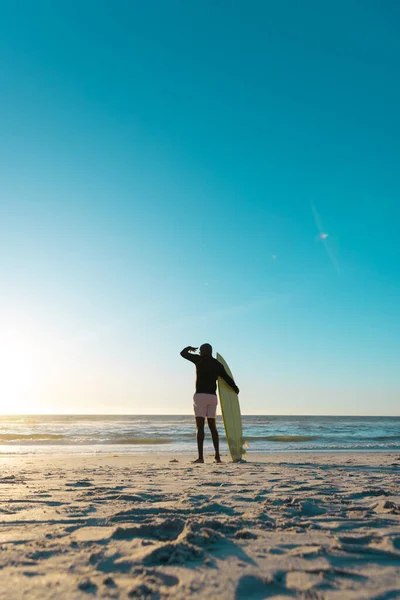 砂浜に立つサーフボードとビューを見てアフリカ系アメリカ人のシニア男性の背面ビュー コピースペース ウォータースポーツ レクリエーション 変更なし 楽しみ 自然海 — ストック写真
