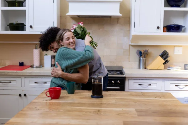 Gülleri Kucaklayan Kocasını Kucaklayan Melez Mutlu Genç Bir Kadın Masada — Stok fotoğraf
