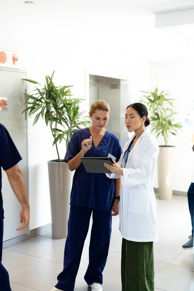 病院の廊下で話してタブレットを持つ2人の多様な女性医師の垂直 コピースペースと 医療サービス — ストック写真