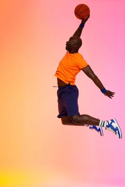 ピンクのバスケットボールでオレンジの背景にジャンプするアフリカ系アメリカ人バスケットボール選手のイメージ スポーツ 競技の概念 — ストック写真