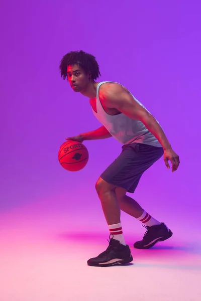 ネオンパープルを背景に バスケットボール選手がバスケットボールを跳ねる姿 スポーツ 競技の概念 — ストック写真