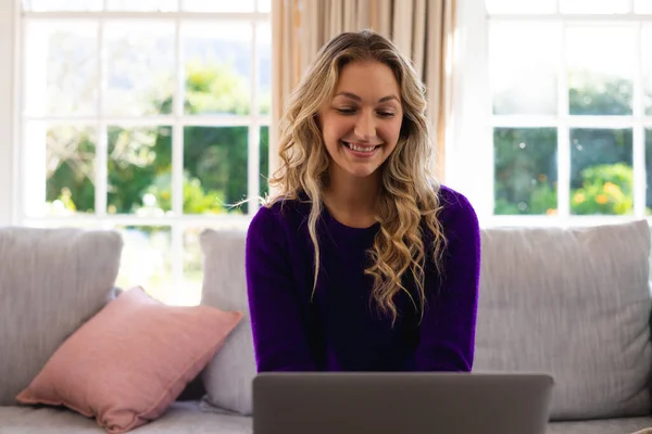 컴퓨터를 사용하는 코카서스 여성을 소파에 앉아서 집에서 일하고 있습니다 긍정적 — 스톡 사진