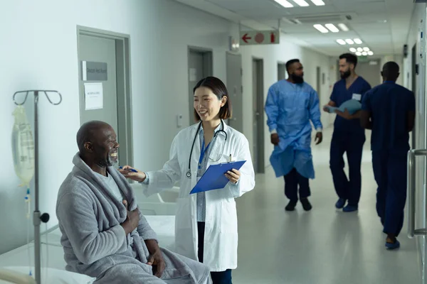 Asian female doctor and senior african american male patient smiling together in hospital corridor. Hospital, medical and healthcare services.