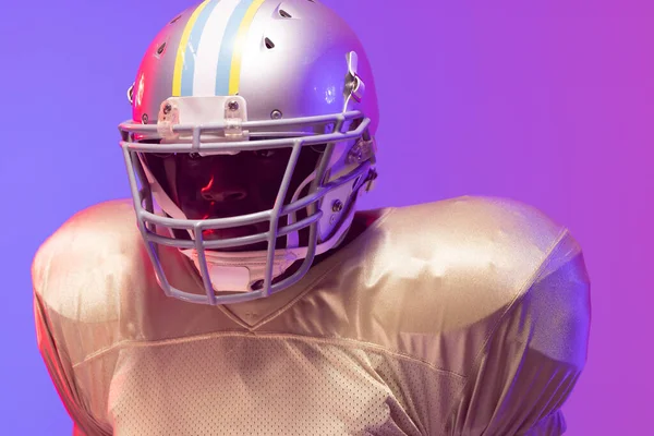 African american male american football player wearing helmet with neon blue and purple lighting. Sport, movement, training and active lifestyle concept.