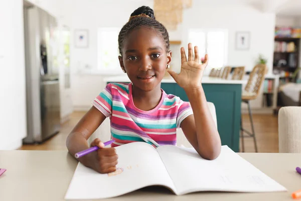 Портрет Афроамериканської Усміхненої Дівчини Махає Рукою Пише Домашнє Завдання Столі — стокове фото